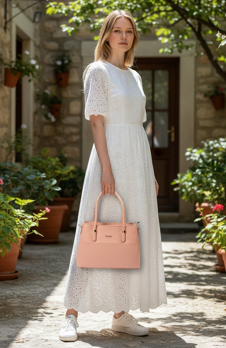 A woman in a white eyelet dress holding a pink medium siddhata PU leather handbag in a stone courtyard.